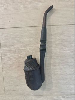 A handcrafted wooden tobacco pipe featuring a carved face or mask on the bowl.
