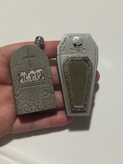 2 goth-style metal coffin-shaped case lighter featuring a raised skull-and-crossbones emblem alongside a matching tombstone-shaped  rip lighter