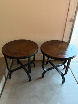 Sturdy end tables have a round wood top with a sunburst veneer pattern and a dark brown finish. The base is constructed from black metal with an X-fra