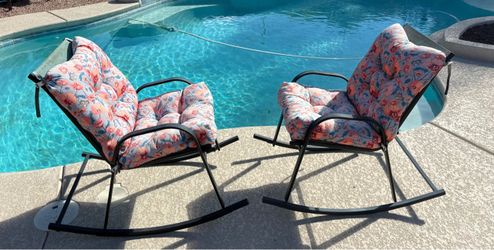 Black metal outdoor rocking chair featuring a plush, coral-toned floral cushion.