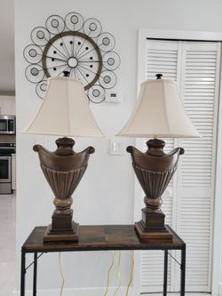 A pair of elegant Regency Hill urn style table lamps. They feature a traditional brown finish, a Roman inspired design with a carved fluted base, and