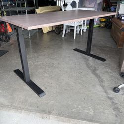 Pneumonic standing work desk gray wood-grain top and black metal T-leg. Has handle to adjust height. Great condition. 60”length. Retails $599