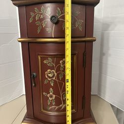 Petite cabinet painted in an exotic red /Brown finish with delicate Oriental rose sprigs. Offers one drawer and one door that opens to a storage compa