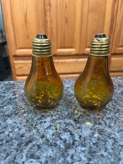 Vintage Amber Glass Light Bulb Pair of Salt and Pepper Shakers. Size approximately 4 1/4 inches tall. Made in Japan. Preowned. One shaker has a d