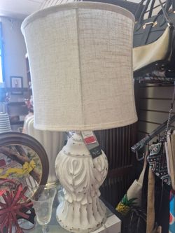 distressed white balustrade table lamp features an acanthus leaf design and a neutral linen drum shade.