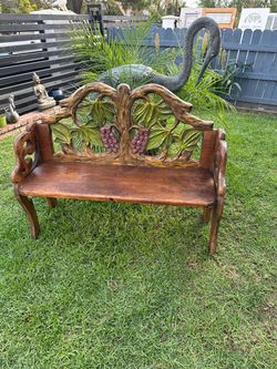 Hand-carved wooden bench has a dark brown finish with green and purple painted accents. This piece features an intricate openwork backrest depicting g