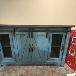 rustic sliding-barn-door console / TV stand, distressed teal base with a dark faux-wood top and mesh side doors