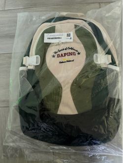 New canvas backpack with a green, cream, and black color scheme. This bag has mesh side pockets, white plastic buckles, and adjustable cream-colored s