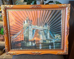 This framed piece is a vintage lenticular or reflective foil print depicting London's Tower Bridge at night with glowing, sunburst-style light rays.