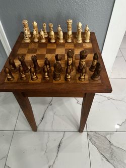 a hand-carved African/Makonde-style figural wooden chess set with a matching wooden chess table/stand. The expressive human-face pieces and carved fig