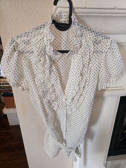 This white and black polka dot blouse features prominent ruffle detailing and a tie-front closure.The blouse is characterized by a sheer, lightweight 