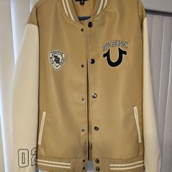 True Religion varsity jacket in tan and Cream . Features bold logo patches and button-up front. Unisex.