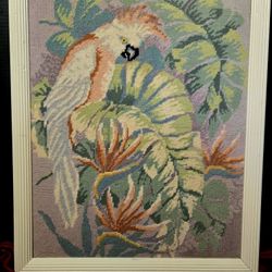Vintage framed needlepoint artwork featuring a cockatoo parrot perched within tropical foliage 18"×22"
