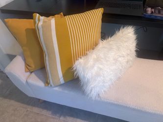 Set of two mustard yellow throw pillows and one white fur.
