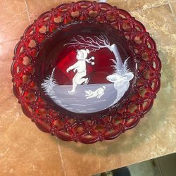This item is a vintage Westmoreland ruby red glass plate featuring a hand-painted "Mary Gregory" style winter scene of a boy ice skating with his dog.