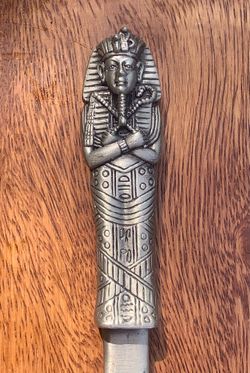 Ancient Egyptian Revival pharaoh letter opener, featuring a metallic handle molded as a mummiform sarcophagus or King Tut figure with hieroglyphic det