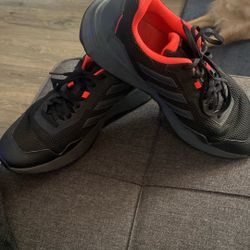 This is an Adidas Tracefinder men's trail running shoe in a black and grey colorway with an orange interior lining. 