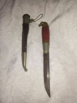 Vintage Finnish puukko knife featuring a traditional cast brass horse-head pommel and a red layered handle, complete with its matching leather sheath.