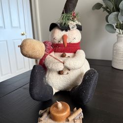 Primitive snowman roasting marshmallow over campfire
