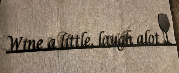 Black Elizabeth Keith metal wall sign with the phrase "Wine a little, laugh alot" and a wine glass shape. 29" L x 6" W