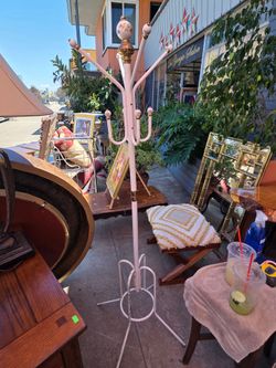 This vintage pink metal freestanding coat rack features ornamental floral porcelain details at the top.