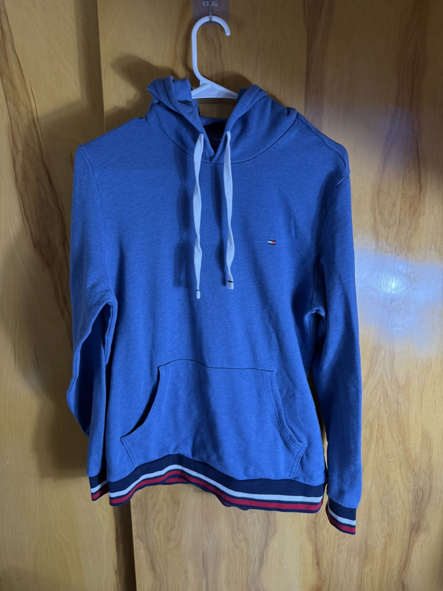 blue Tommy Hilfiger hoodie with a small flag logo embroidery and signature red, white, and blue stripe details on the hem
