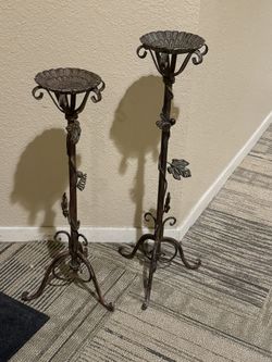 Set of two ornate metal candle or small plant holder stands with leaf and vine design.