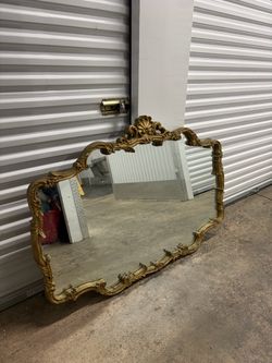 A vintage large wall mirror in a carved gilded frame in the Baroque/Rococo style, with a lavish ornament and a central cartouche/shell on top.
