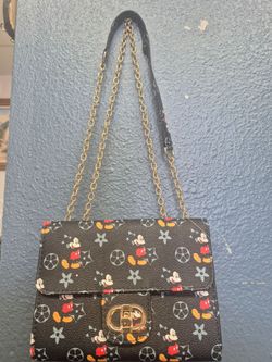 black crossbody bag features a playful Mickey Mouse monogram pattern and a gold-tone chain strap..