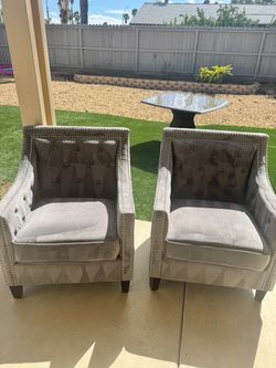 Gray tufted accent chairs with silver nailhead trim and diamond stitching