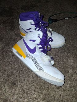 These are Nike Air Jordan Legacy 312 "Lakers" sneakers, identifiable by their purple swoosh, yellow heel accent, and distinctive elephant print mudgua