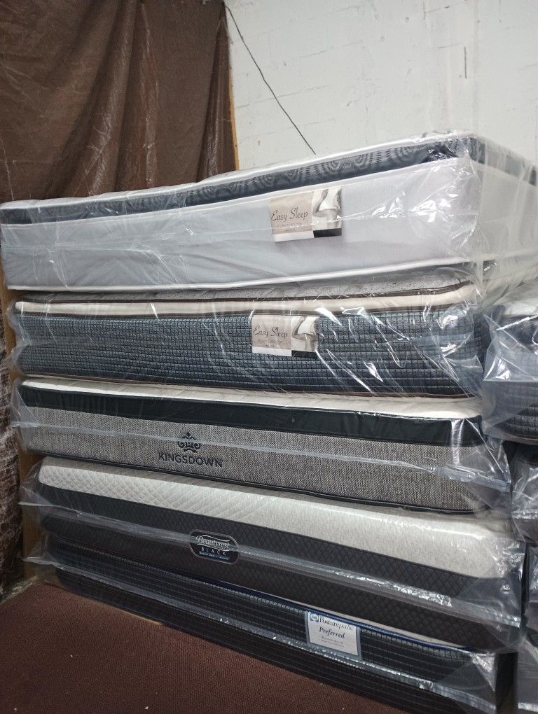Have All Size Available Good Prices Todos Los tamaños Disponibles Stack of new mattresses wrapped in protective plastic. Multiple styles available.