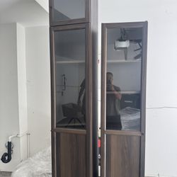 Description: Two tall matching display/storage cabinets in a dark walnut wood finish with glass doors. Each unit has adjustable shelves and plenty of 