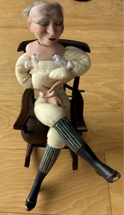 Porcelain doll in wood rocking chair to finish. 12” tall in sitting position snd 5” wide.
