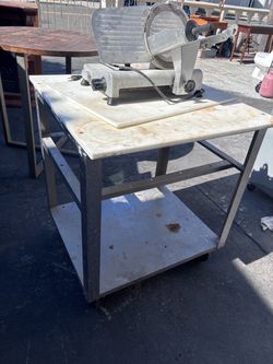 Meat slicer with stainless steel cutting board table on wheel.s