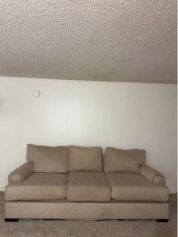 Comfortable three-seater sofa has beige fabric upholstery. This couch is designed with rolled arms and classic nailhead trim. The piece includes three