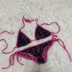 Two-piece string bikini with triangle top and tie-side bottoms. Hot pink trim and zebra-inspired animal print with dark sequin overlay. Bold, playful 