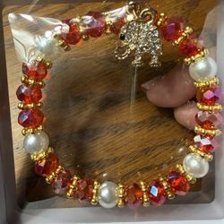 Brand new stretc charm bracelet featuring red faceted beads, white faux pearls, gold-toned spacers, and an elephant charm. Such beaded accessories are