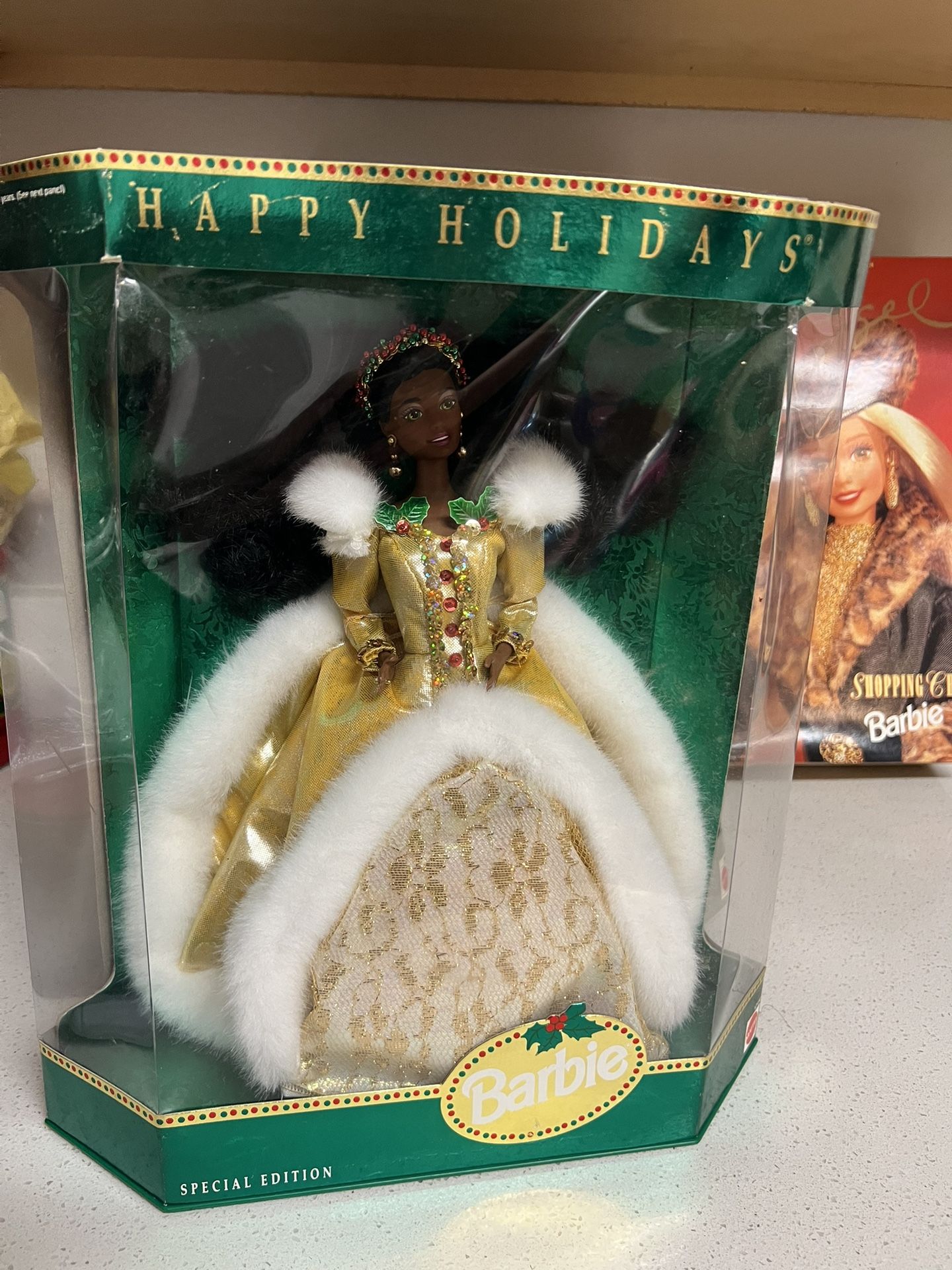 1994 Happy Holidays Special Edition African American Barbie Doll. The doll wears a glamorous, faux fur-trimmed golden dress with a white and golden l