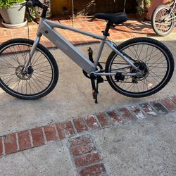 The image shows a GenZe Sport e101 electric bike.  It features a 250-watt geared rear hub motor. The bike has a 7-speed Shimano drivetrain and Promax 