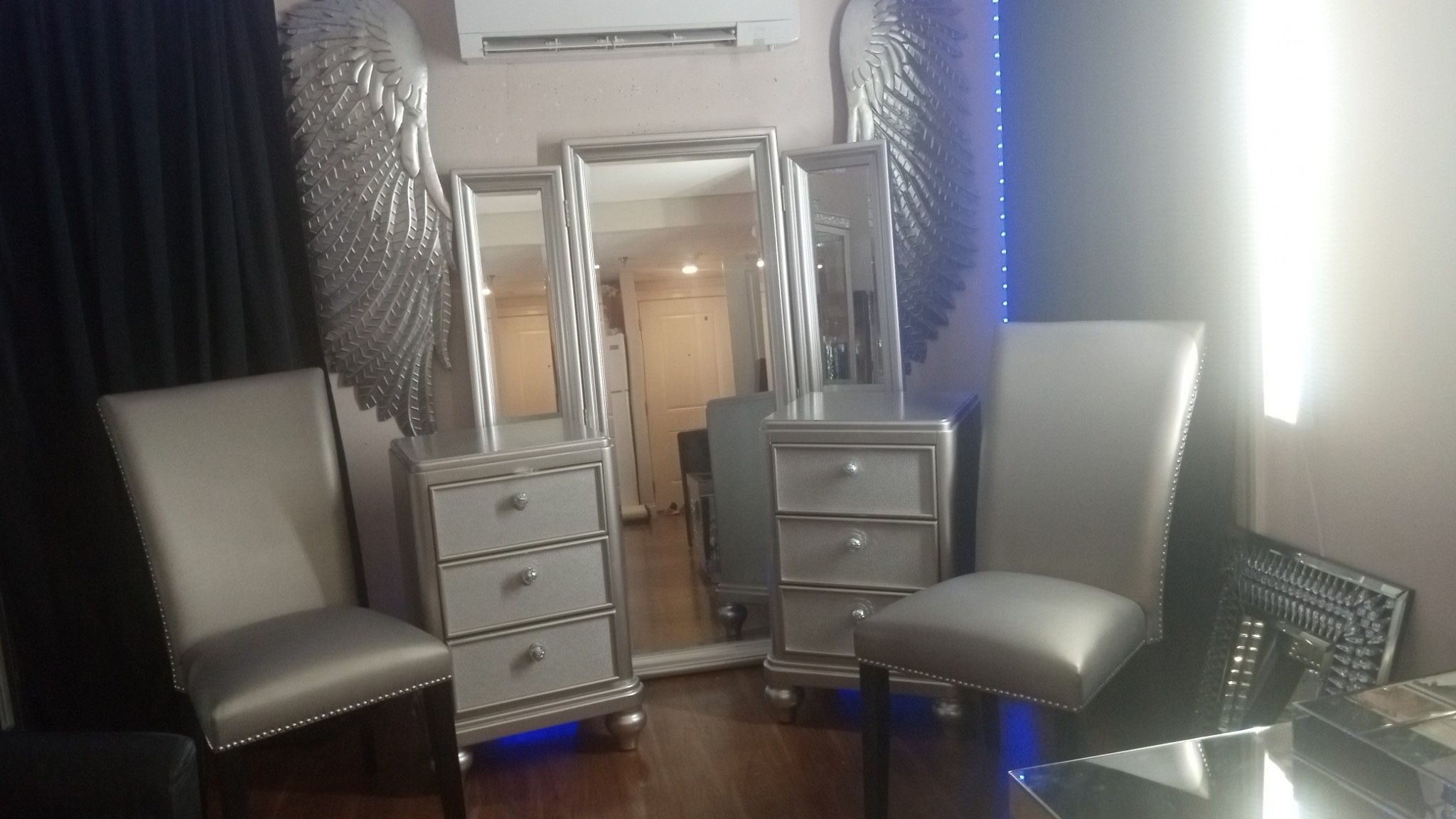 Two silver chairs long mirror with two attached mirrors. And two nightstands.