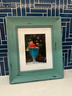 "Sugarbird Cocktail" with little birds perched on a blue drink with teal frame
