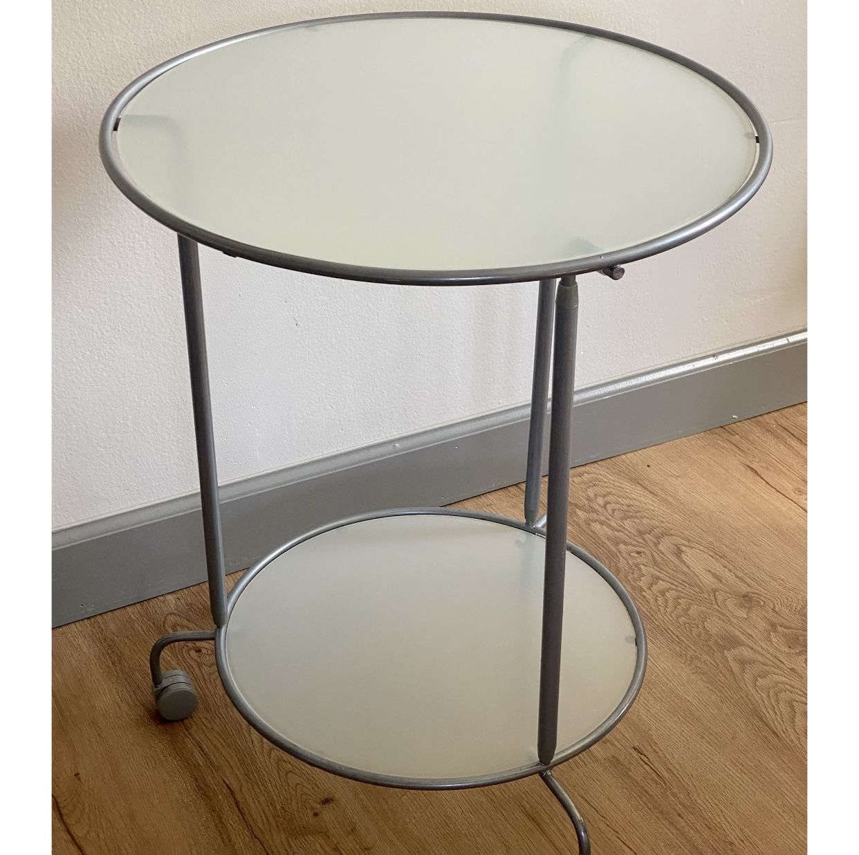 IKEA Heimdal glass and metal rolling side table. The top shelf is 19.5" in diameter and the bottom shelf is 16" in diameter. It is 24" tall