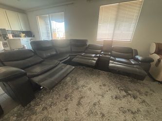 grey faux leather power reclining sectional sofa with a built-in storage console and cup holders.