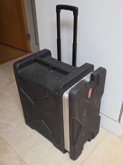 SKB rolling roto-molded rack case, featuring a heavy-duty hard plastic shell, a retractable pull handle, and integrated wheels for transporting audio,