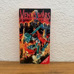 The Venus Wars VHS featuring red cover art. Bright red and black artwork highlights the sci-fi action theme. Compact retail packaging ideal for collec