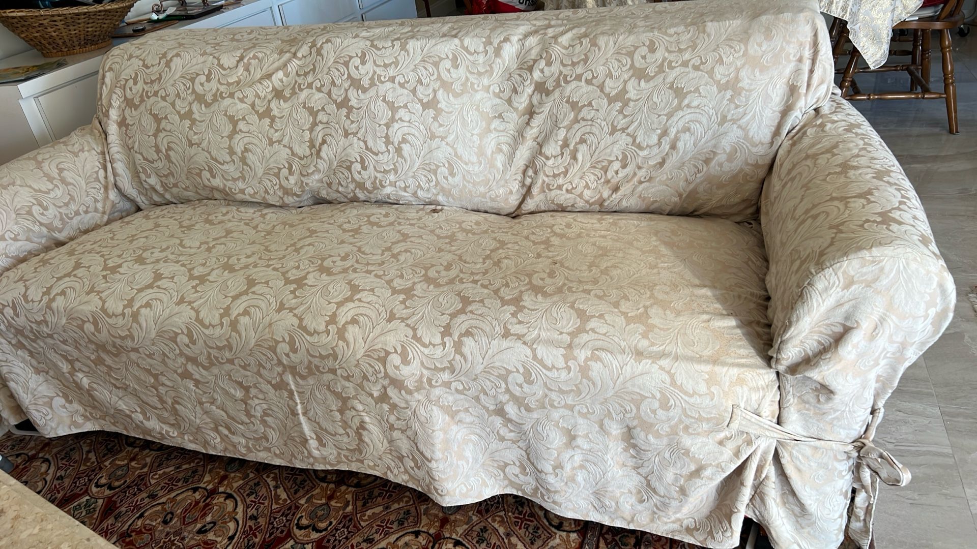 sofa slipcover with a damask or brocade pattern in a light beige or champagne color.