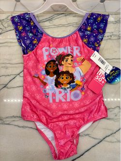 colorful girls one-piece swimsuit. Has Disney Encanto characters Mirabel, Luisa, and Isabela on front with text 'POWER TRIO'. Pink body with purple bu