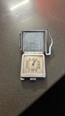 Este es un reloj de cartera Art Déco vintage, posiblemente de la marca Mimo o Gruen, caracterizado por su diseño plegable funcional.El objeto cuenta c
