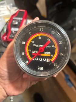 Vintage Western Flyer bicycle speedometer with a black plastic housing and a clear lens. This mechanical gauge includes a drive cable and features a r